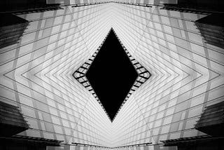 Abstract black-and-white architectural image with mirrored geometric lines converging toward a dark central space, symbolising hidden structures, paradigms, and the unseen patterns that shape how people interpret reality.