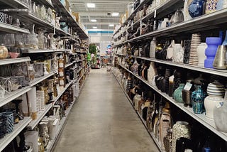 Looking down the isle in a big-box store. Miscelleneous decorative household items line the shelves on each side.