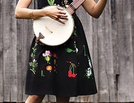 Rhiannon Giddens with a banjo in front of a barn.