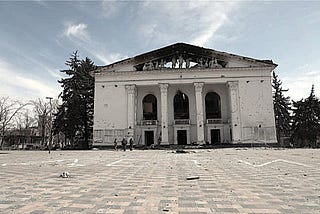 Image of the Donetsk Academic Regional Drama Theatre in Ukraine, destroyed by the Russians in 2022, with the Russian word for “children” written in front of it in large, white Cyrillic letters.