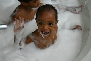 Baby Nathan waving in his bubble bath as a one year old baby