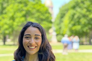 Marla standing in the greenery of her campus wearing a grey suit.