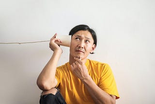 Man trying to listen to something with a paper cup and string