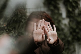 A young woman has her hands outstretched in front of her face, with her palms facing forward. The image focuses on her palms while the rest is blurred.