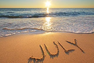 A beach, the sea and “July” written on the sand