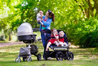 A mother walking with her kids in baby strollers.