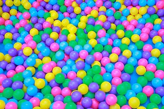 A close shot of a ball pit filled with bright pink, purple, blue, green and yellow balls.