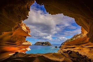 From the inside of a cave, a small island sits a short distance away