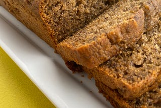 Gluten free banana bread, with 3 slices cut sitting on a white plate. bright yellow brackground.