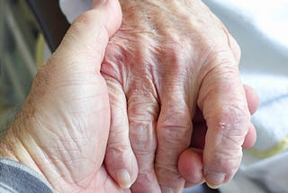 Close-up of elderly woman holding hands with another person.