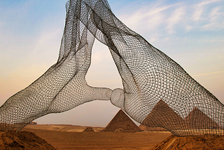 A silhouette of hands in a mudra gesture, resembling a massive wire statue towering over the pyramids in the desert.