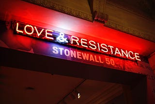 Red-lit marquis with neon text “LOVE & RESISTANCE” over white text reading “Stonewall 50”