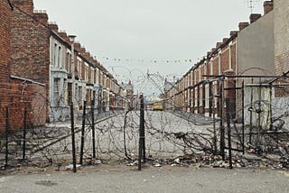 View of a hastily constructed barbed wire fence that runs across a terraced street to mark a peace line or dividing line between republican and neighbouring loyalist areas of Belfast, Northern Ireland during The Troubles in April 1972.