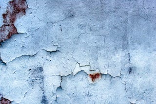 White plaster, interspersed with red rusty blotches, peeling off an exterior wall.