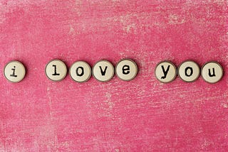 buttons spelling out ‘i love you’ on a pink background