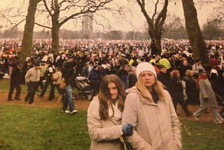 Huge crowd of people in Hyde Park, amongst trees and grass. Young India and her Mum stand in front looking at camera.