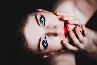 A woman with ocean blue eyes and, crimson colored lips looking up to the camera.