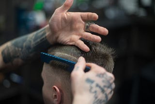 Photo of a young man getting a haircut by a tattooed barber.