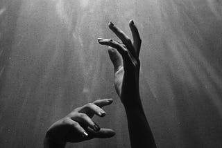 Black and white photo with hands reaching up to light shining down.