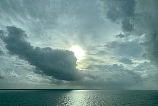 open ocean, clouds backlit by sun, light on water, greys, blues