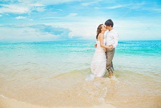 A happy couple kisses on the beach after getting married