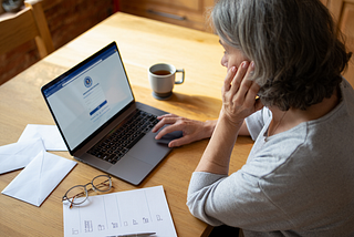 A woman sits at a table and stares at a laptop.