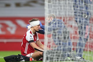 David Luiz (left) is being assisted by Arsenal’s senior physio, Jordan Reece, after suffering a head to head collision.