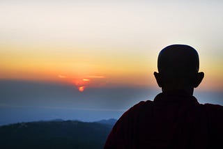 Buddhist Monk looking at a sunset with his head bowed