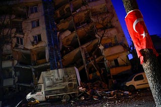 A Turkish flag is seen on a pole in front of a collapsed building, as rescue continues in the aftermath of a deadly earthquake in Kahramanmaras, Turkey February 12, 2023. REUTERS/Guglielmo Mangiapane