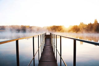 Bridge over foggy water at sunrise