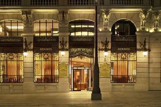 a view from the outside of hermes store at night, grated windows, with wooden wardrobes back to them