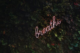 a neon breathe sign on top of a leafy background