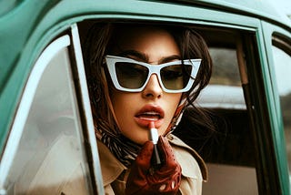 Woman reapplying lipstick, wearing sunglasses