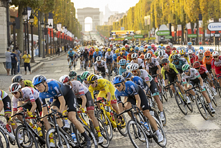 A peloton of cyclists rides through a road and the Arc de Triomphe in the background.