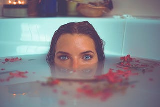 woman in bathtub with red flower petals floating on water. Photo by Timothy Dykes on Unsplash