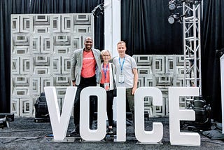 Guy, Polina and Tim are standing on stage of the voice summit posing with the big letters which say “voice”