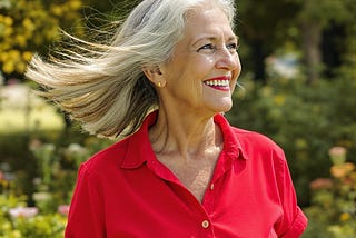 Older woman, gray hair blowing in the breeze, face and neck wrinkles, smiling in nature