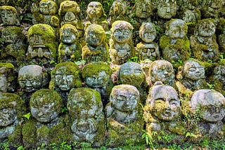 Rows of small stone statues covered in moss, set into a wooded hillside at Daikaku-ji Temple in Kyoto.
