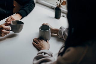 Priscilla Du Preez took this photo of the hands of two women sitting at a table holding coffee cups.