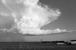 Black and white photo of an enormous cloud coming down and taking over the skyline towards the highway.