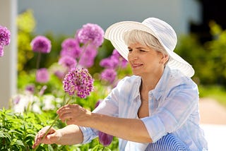 n older grey haired woman standing by purple flowers and smiling friendship death seniors