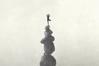 A woman balancing on top of 5 stacked rocks.
