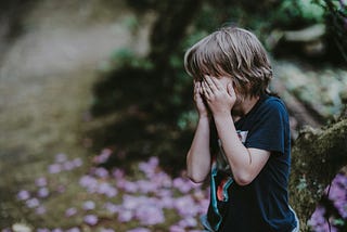 Boy blue shirt hands over eyes in garden purple flowers