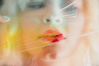 Blond woman behind a sheet of plastic, lipstick smeared.