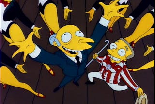 A screenshot of The Simpsons depicting Burns and Smithers from a high angle. Mr. Burns holds his hands up above his head and smiles widely, while Smithers kneels beside him and grins. Smithers is wearing a red-and-white suit, holding a cane in one hand and a hat in the other.