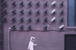 man walking wearing white with a mask under an installation of surveillance cameras
