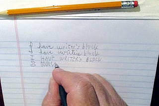 Hand with pencil and pad writing “I have writer’s block” over and over