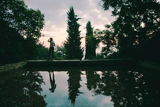 A girl looking at the sunset reflected on water and surrounded by trees