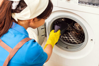 Image showing a girl with blue top scrubbing the inside of a washing machine drum with a sponge and cleaning solution.