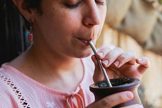 woman in pink shirt, eyes closed drinking brown mug with metal silver straw